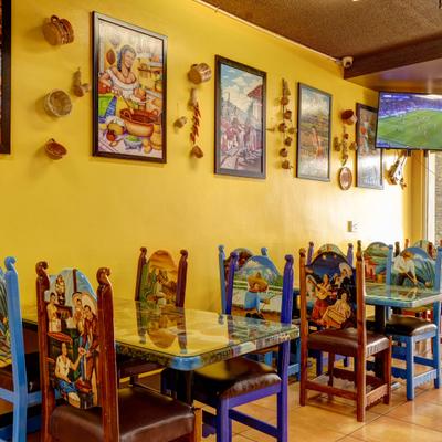 Mexican restaurant interior with tables, colorful hand-painted chairs and wall art.