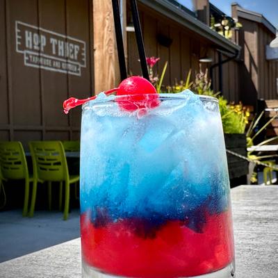 Red and blue drink topped with a cherry, served on a table outside.