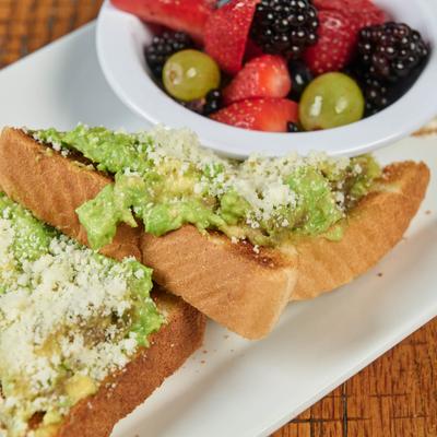 Avocado toast with crumbled cheese; bowl of mixed fruits and a fried egg on a plate