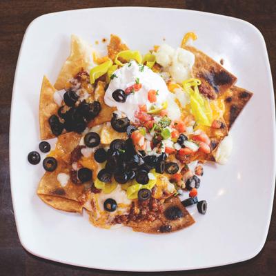 A plate of nachos topped with melted cheese, sour cream, black olives, diced tomatoes & jalapeños