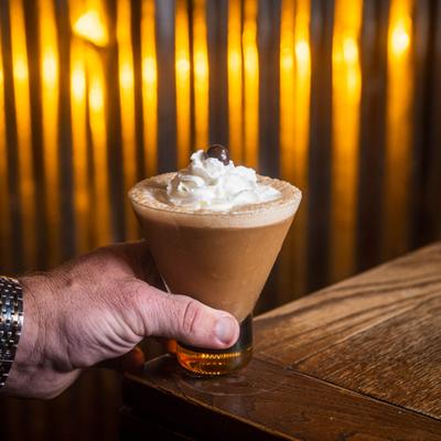 Hand holding a chocolate martini topped with whipped cream and a cherry.