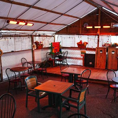 Outdoor dining tent with tables, chairs, heaters, and flowers.