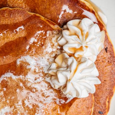 Pancakes topped with melting butter, syrup and whipped cream, close-up.