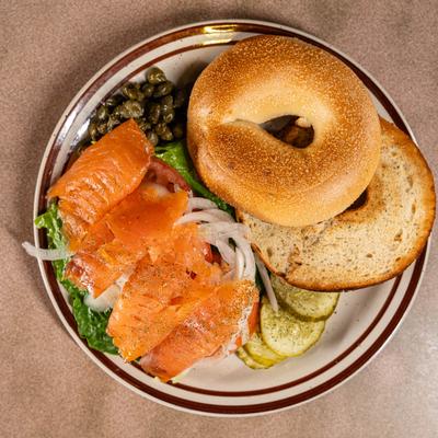 Toasted bagel with smoked salmon, capers, onions, and lettuce on a plate.