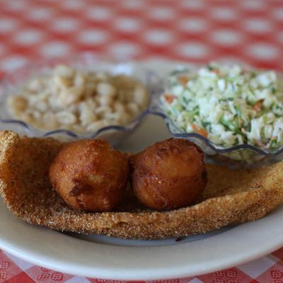 Fried fish with hush puppies on top, sides of white beans and coleslaw.