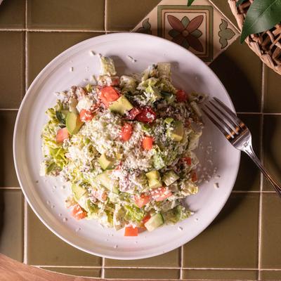 Mexican Chop Salad, with lettuce, bacon, avocado, egg, onion, tomato, cucumber, and cheese.