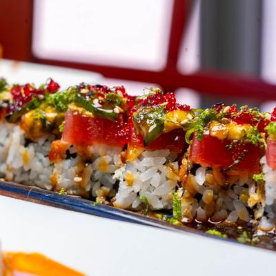 A close-up of a sushi roll topped with tuna, roe, and herbs.