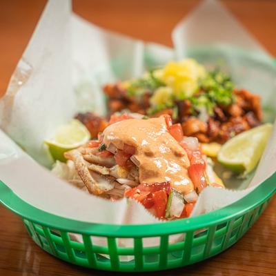 An order of fish tacos served in a green basket.