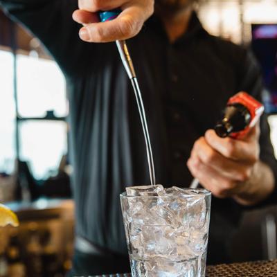 Bartender pouring a drink into a glass with ice cubes