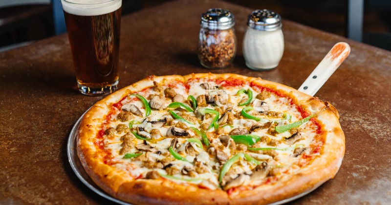 Pizza topped with mushrooms and peppers, served on the table with a glass of beer