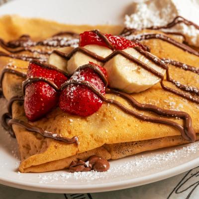 Crepe topped with strawberries, banana slices and chocolate sauce drizzle.
