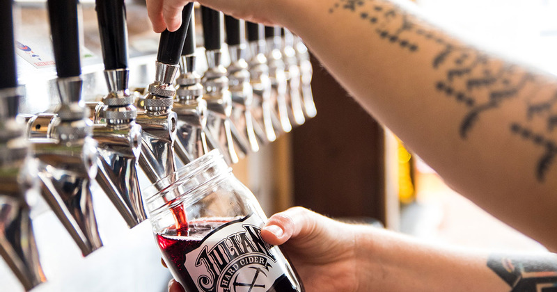 Closeup of bartender's hands pouring cider from a tap into a glass jar