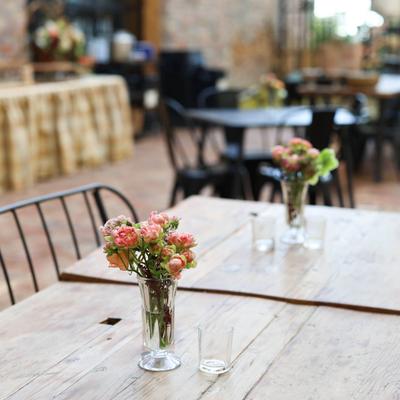 Small flower arrangements on wooden tables in outdoor patio setting.