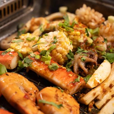 Variety of seafood and vegetables being cooked on a table-top grill.