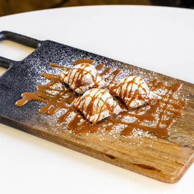 Three powdered raviolis topped with caramel drizzle on a wooden board.