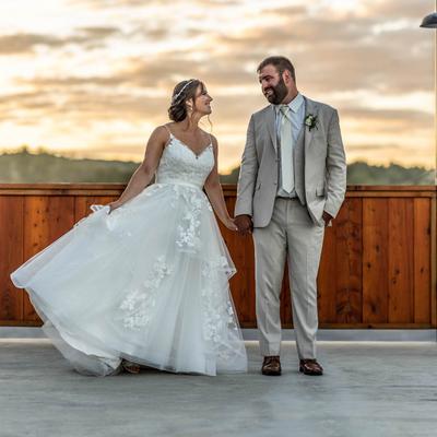 A bride and a groom smiling and looking at each other, standing outside at sunset.