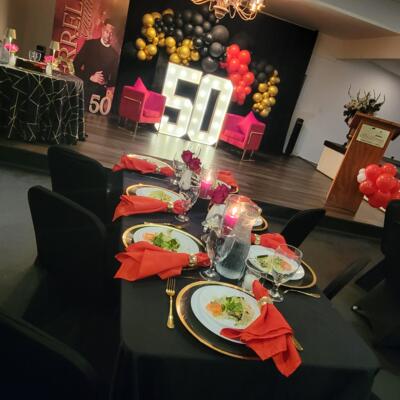 Elegant 50th birthday party setup with black tables, red napkins, and marquee lights.