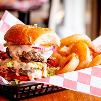 Double cheeseburger with crispy onion rings in a basket.