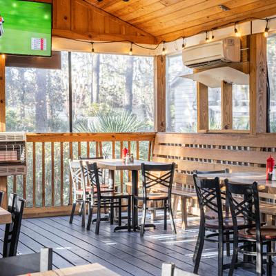 Covered outdoor patio seating with tables, chairs and a TV screen.
