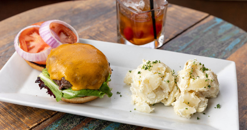 The Lula Burger served with potato salad, accompanied by a glass of cocktail