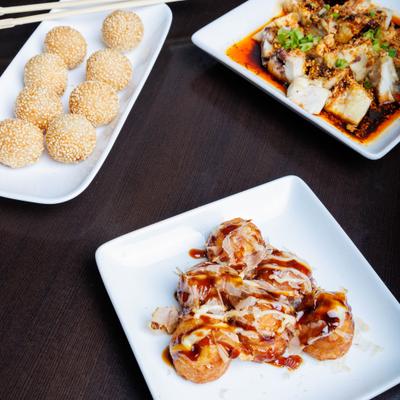Assorted Asian appetizers including sesame balls, spicy chicken, and takoyaki.
