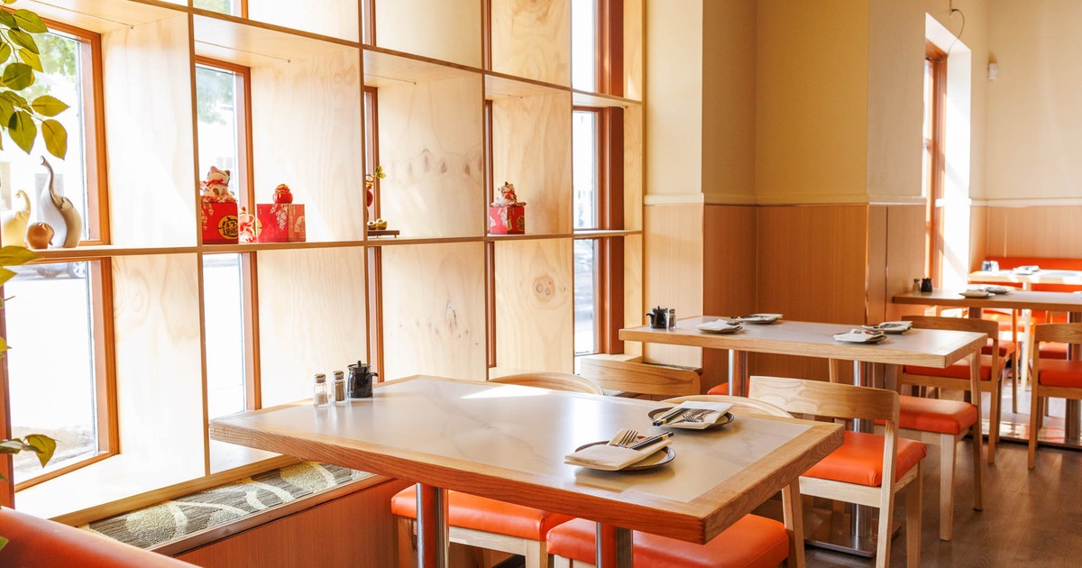 Interior with wooden tables, orange cushioned chairs, and decorative shelving by the windows.