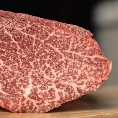A raw beef steak placed on a wooden cutting board, showcasing its rich red color and marbling.