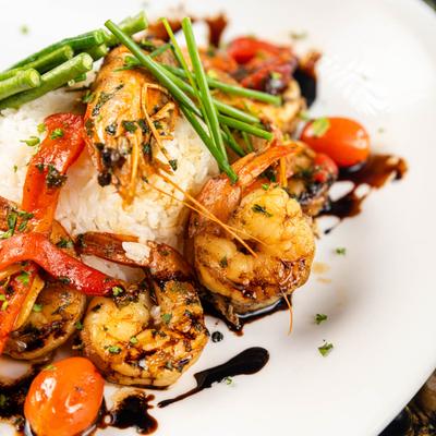 Grilled shrimp dish with rice, vegetables, and balsamic glaze.