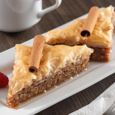 Two triangular pieces of baklava topped with cinnamon sticks on a white plate.