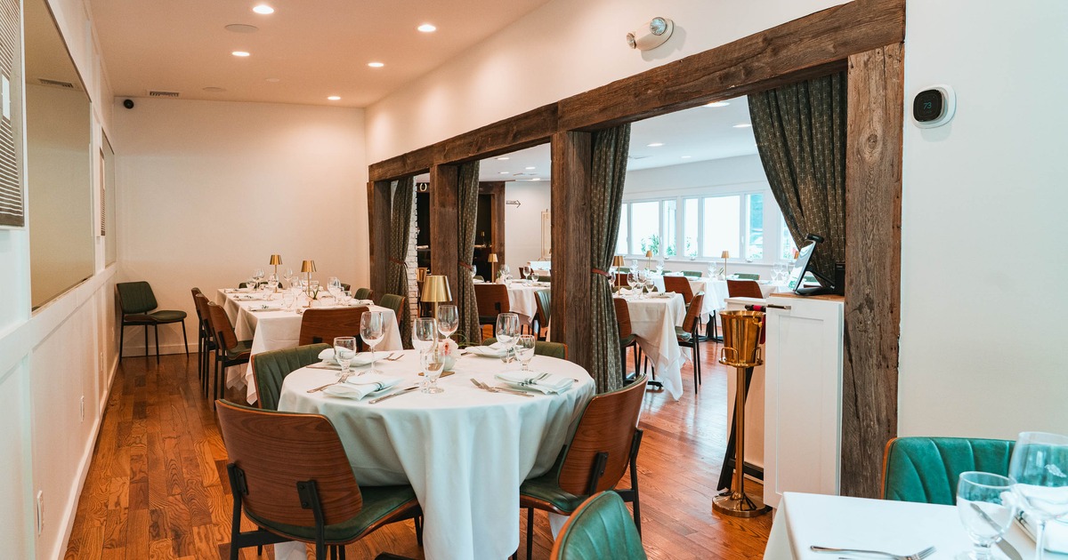 Elegant fine dining restaurant interior with white tablecloths, wood floors, and soft lighting