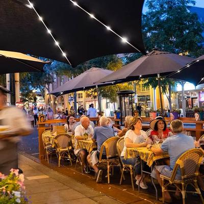 Busy outdoor restaurant seating at dusk under string lights with diners.