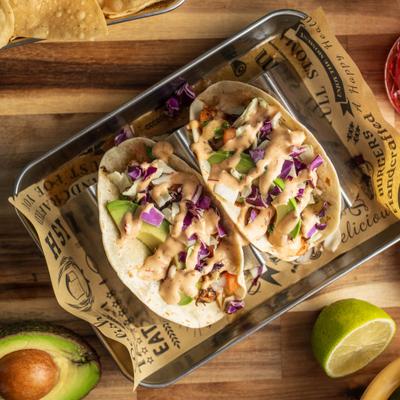 Shrimp Tacos topped with slaw, avocado slices, and chipotle aioli, served on a tray.