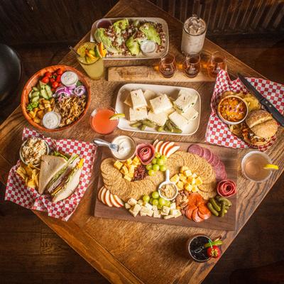 Charcuterie board surrounded by plated dishes and drinks on a wooden table.