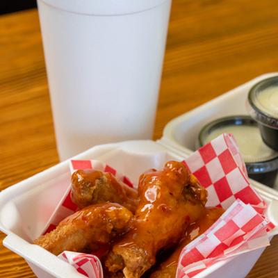 Buffalo wings served in a takeout container with cups of dipping sauce.