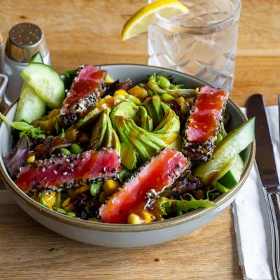 Bowl of Seared Ahi Cafe Salad, served on the table with a drink.