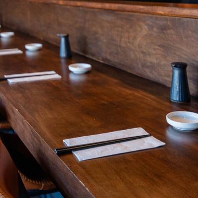 Wooden sushi counter set with chopsticks, ceramic plates, and soy sauce bottles.