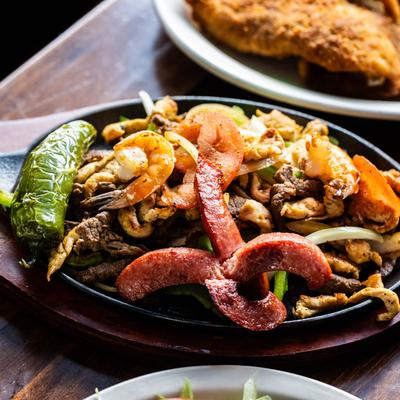 Mixed grill platter with beef, shrimp, sausages, and vegetables.