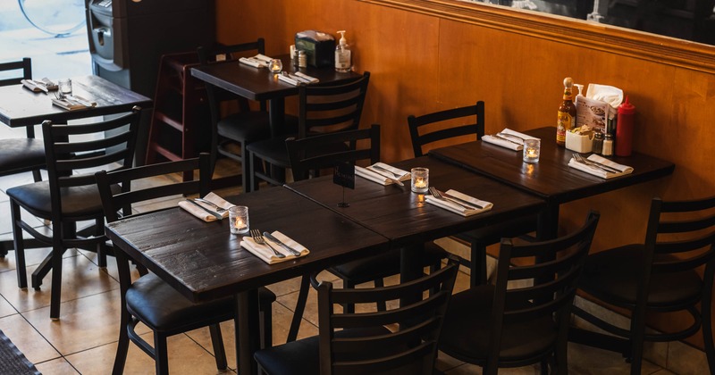 Interior with dark wooden tables, black chairs and lit candles.