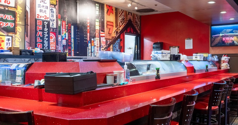 Interior of a sushi bar with a red counter and cityscape wall decor.