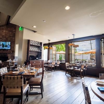 Interior with tables, wood floor, view of outside seating area through windows.