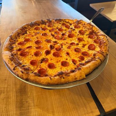 Pepperoni Pizza served on a metal pizza pan atop a wooden table.
