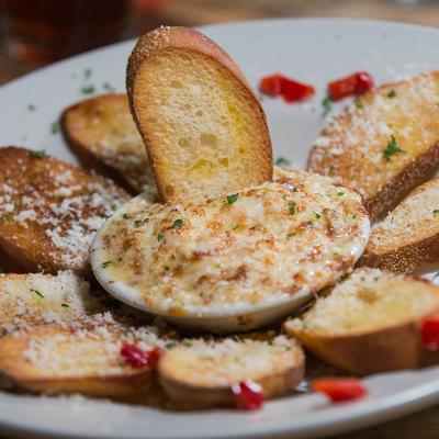 A plate with cheesy baked dip surrounded by crispy toasted baguette slices.