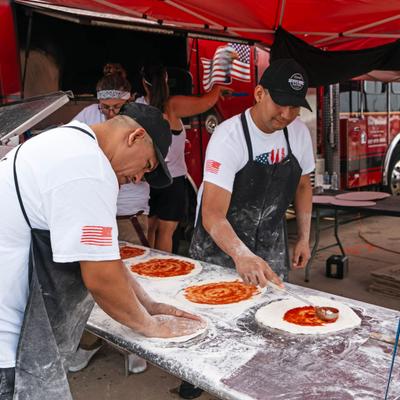 Pizza chefs stretching dough and spreading marinara sauce over it.
