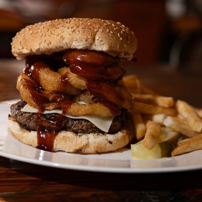BBQ burger with onion rings, served with fries and a pickle.