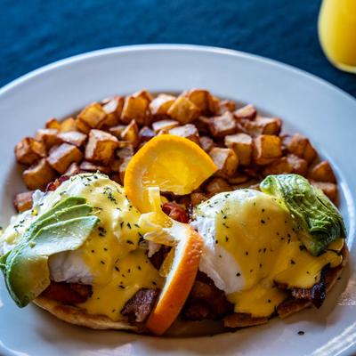 California Benedict with bacon, tomato, avocado, two poached eggs, and potatoes.