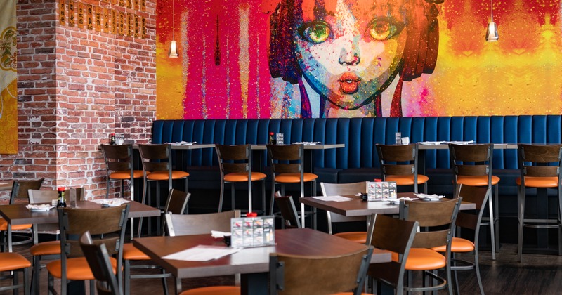 Interior, dining tables, banquette seating by a wall with large mural art