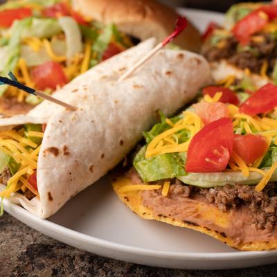 Taco and tostada plate featuring toppings of ground beef, cheese, lettuce and tomato.