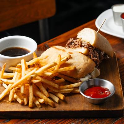 Beef and cheese sandwich with fries, ketchup, and French dip on a board.