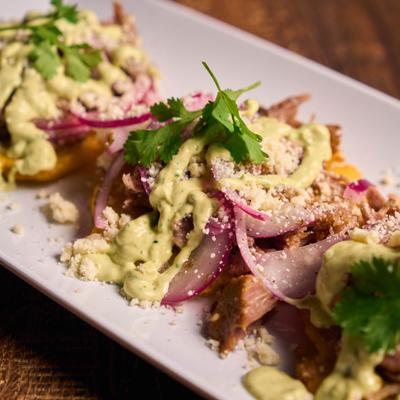 Twice-fried green plantains topped with shredded meat, pickled onions, and aioli.