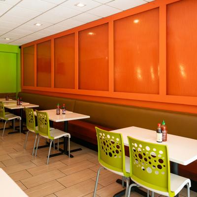 Dining room with green chairs, white tables and large, bright orange wall panels.